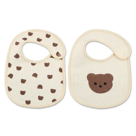 A set of two baby bibs made of soft fabric. One bib features a repeating pattern of small brown bear faces, while the other showcases a single large brown bear face in the center. Both bibs have a neutral beige background with a rounded shape and a side closure for easy wear.