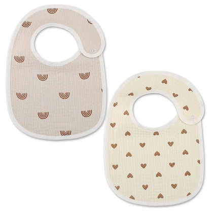 A set of two baby bibs made of soft fabric. One bib features a pattern of small brown rainbows on a beige background, while the other has a design of tiny brown hearts on a light cream background. Both bibs have a rounded shape and a side closure for easy use.