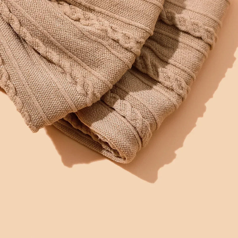 Close-up detail of textured beige cotton bow showing delicate ribbed fabric pattern and gentle pleating, photographed with natural shadows on warm beige background to highlight the handcrafted construction and premium material quality