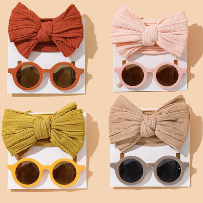 Complete collection of baby accessories featuring four coordinating bow and sunglasses sets: terracotta red with matching frames, soft blush pink with pink frames, mustard yellow with yellow frames, and classic beige with gray frames, elegantly arranged on white cards against a warm beige background