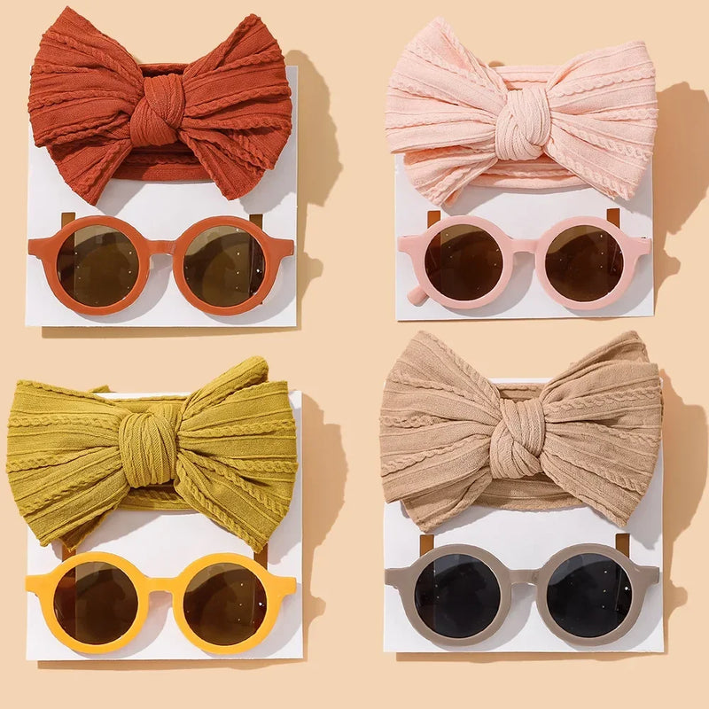 Complete collection of baby accessories featuring four coordinating bow and sunglasses sets: terracotta red with matching frames, soft blush pink with pink frames, mustard yellow with yellow frames, and classic beige with gray frames, elegantly arranged on white cards against a warm beige background