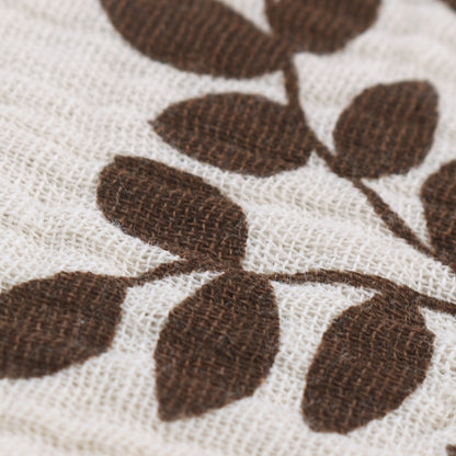 Close-up texture detail of quilted baby towel featuring rich brown leaf pattern embroidered on cream textured cotton, showcasing the intricate weave and high-quality fabric construction