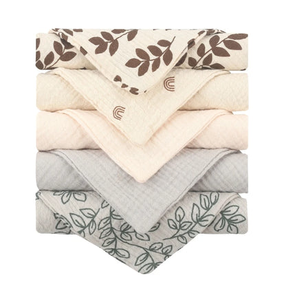 Collection of quilted baby towels featuring cream towels with brown leaf patterns and rainbow motifs, solid cream towels, and grey towels with delicate botanical line drawings, all with diamond-textured cotton for gentle baby care