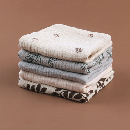 Stack of quilted baby towels in soft neutral tones featuring delicate botanical prints in brown and gray, with diamond-textured cotton for luxurious softness and absorbency, perfect for gentle baby care