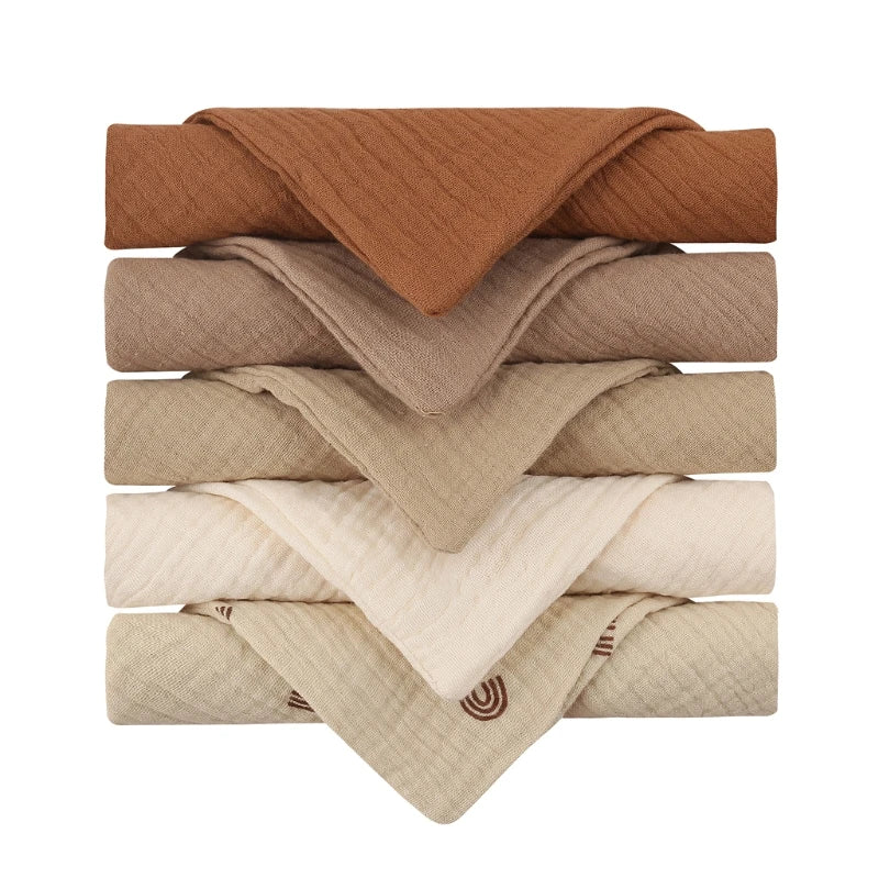 Collection of quilted baby towels in warm earth tones, graduating from rich terracotta brown through taupe to cream, with a decorative rainbow pattern on the bottom towel, all featuring diamond-textured cotton for luxurious baby care