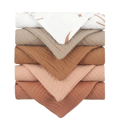 Collection of soft baby towels stacked in harmonious earth tones, ranging from white to beige, taupe, caramel, and terracotta, featuring gentle textured cotton material perfect for drying and comforting baby after bath time