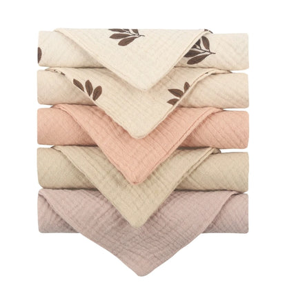 Collection of quilted baby towels in neutral tones featuring cream towels with delicate brown leaf prints, complemented by solid towels in soft pink, beige, and taupe, all with diamond-textured cotton for gentle baby care