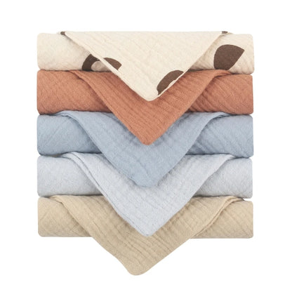 Collection of quilted baby towels featuring a cream towel with brown dots, complemented by solid towels in terracotta, soft blue, light grey, and beige, each with diamond-textured cotton for gentle baby skincare