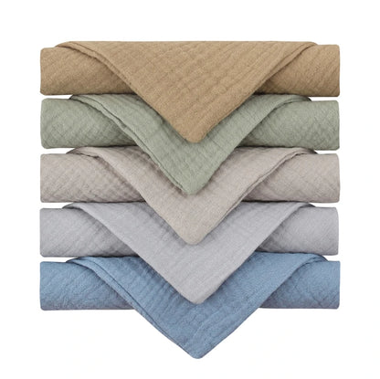 Collection of quilted baby towels stacked in calming neutral colors, ranging from warm beige, sage green, light taupe, dove grey to soft blue, featuring a textured diamond pattern perfect for gentle drying and post-bath comfort