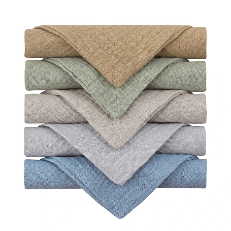 Collection of quilted baby towels stacked in calming neutral colors, ranging from warm beige, sage green, light taupe, dove grey to soft blue, featuring a textured diamond pattern perfect for gentle drying and post-bath comfort