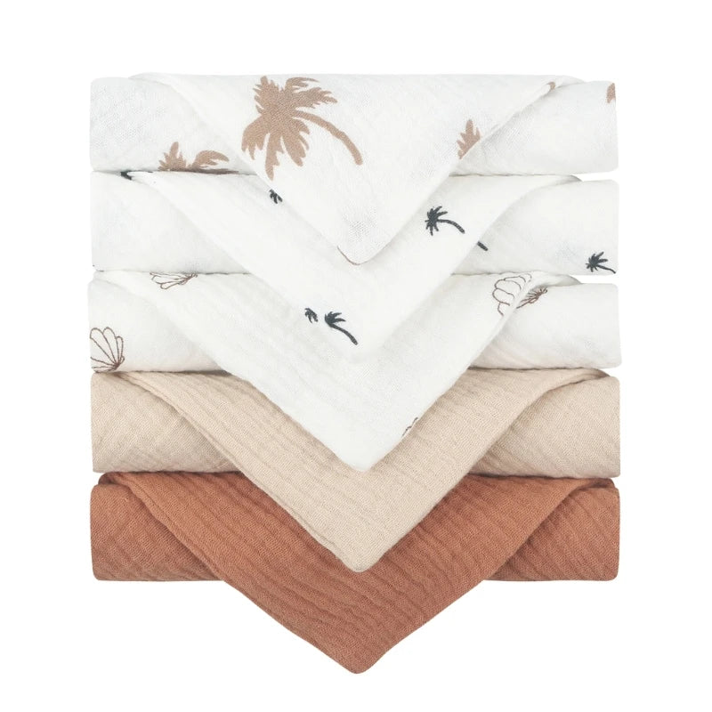 Collection of quilted baby towels featuring white towels with delicate brown palm tree prints, complemented by solid towels in beige and terracotta, all with diamond-textured cotton for gentle and absorbent baby care