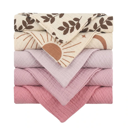 Collection of quilted baby towels featuring decorative cream towels with brown leaf prints and sunrise patterns, complemented by solid towels in graduated pink tones from light to rose, all with diamond-textured cotton for luxurious baby care