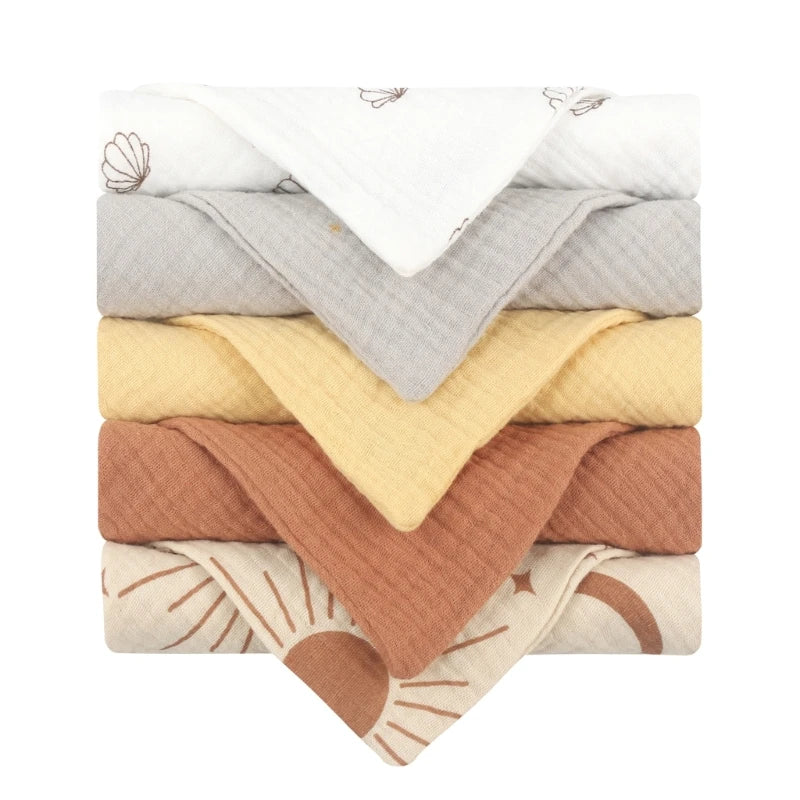 Collection of quilted baby towels featuring a cream towel with seashell and sunrise designs, complemented by solid towels in terracotta, soft yellow, and light grey, each with diamond-textured cotton for gentle after-bath care