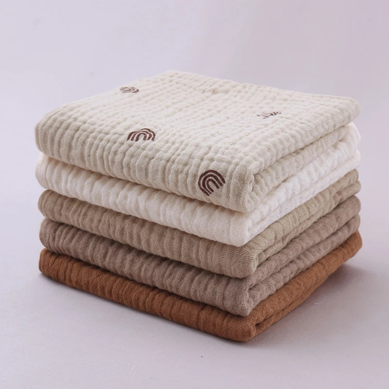 Stack of quilted baby towels in a soothing gradient from cream to rich terracotta, featuring delicate seashell embroidery details and diamond-textured cotton, combining both style and softness for gentle baby care