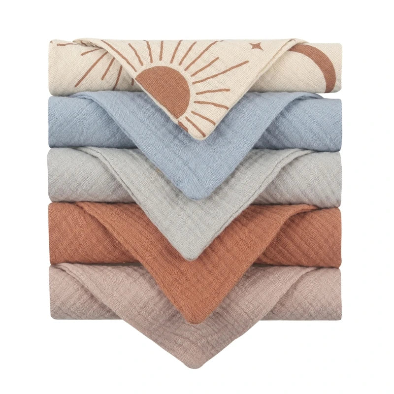 Collection of quilted baby towels featuring a decorative sunrise pattern on cream fabric, stacked with coordinating solid towels in soft blue, light grey, terracotta, and beige, showcasing diamond-textured cotton perfect for gentle baby care