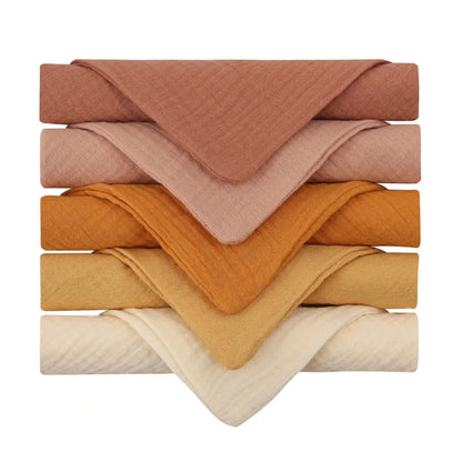 Collection of quilted baby towels in warm earth tones, featuring a gradient from deep terracotta through rust orange to soft yellow and cream, each towel with diamond-textured cotton for gentle and cozy baby care