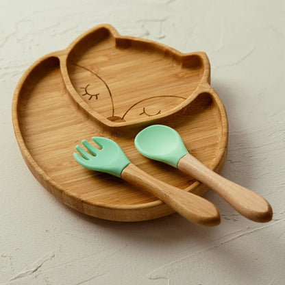 Bamboo fox-shaped baby plate with divided sections, paired with a wooden spoon and fork featuring green silicone tips, designed for safe toddler meals and baby-led weaning.