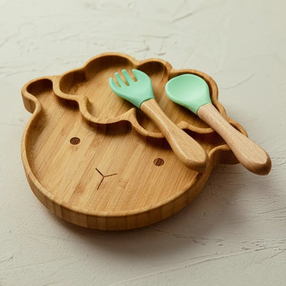 Bamboo sheep-shaped baby plate accompanied by a wooden spoon and fork with green silicone tips, designed for toddler meals and baby-led weaning.