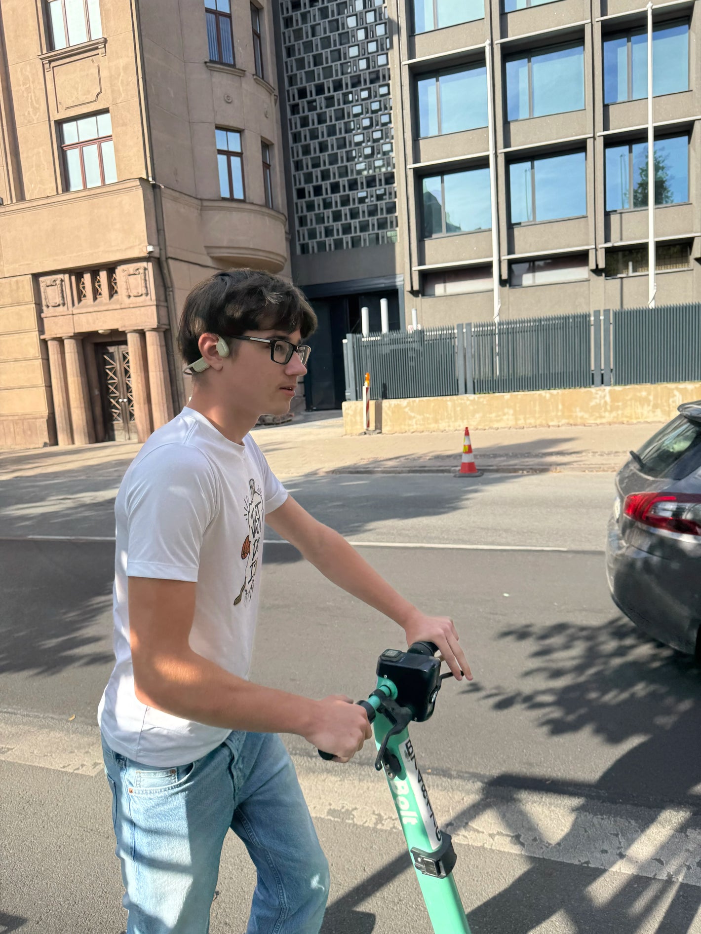 A boy is aware of his surroundings in traffic while wearing open-ear bone conduction headphones on a road.