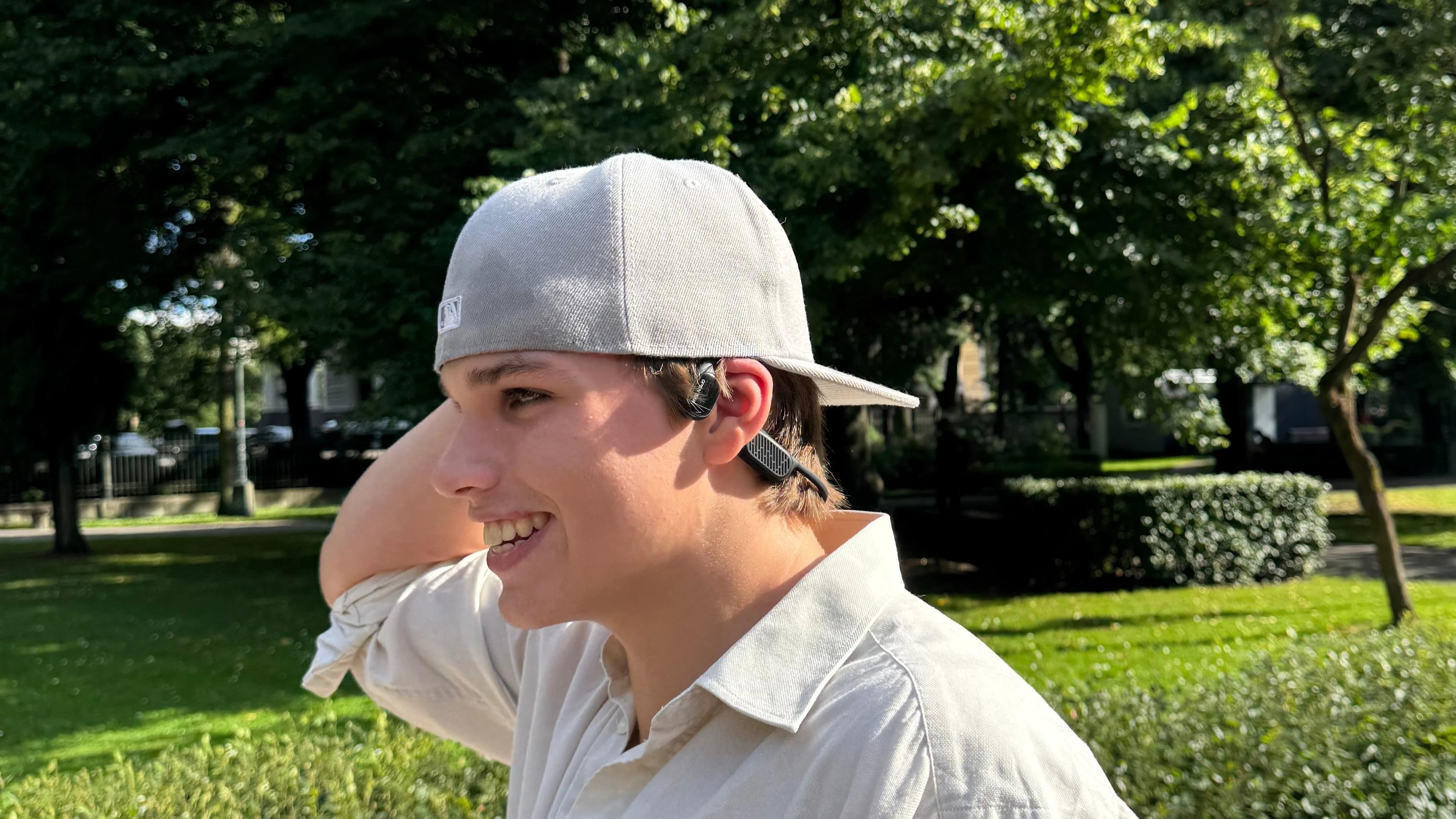 A boy wearing a cap and open-ear bone conduction headphones.
