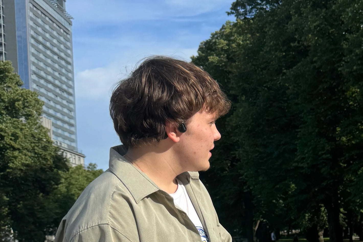 A boy with long hair wearing open-ear bone conduction headphones.