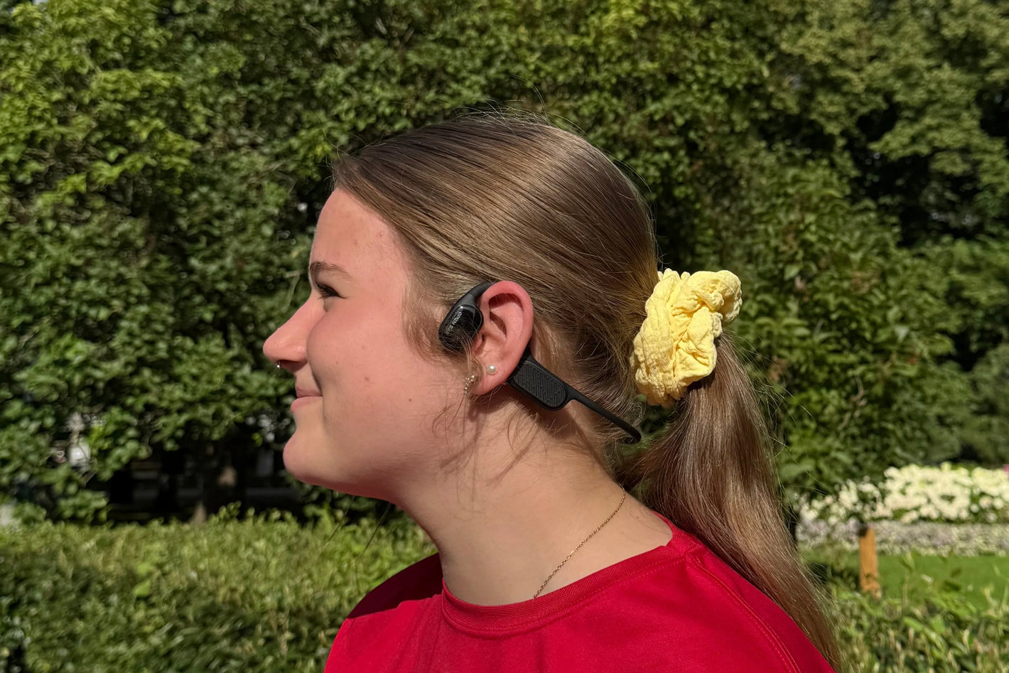 A girl in a red shirt wearing open-ear bone conduction headphones.