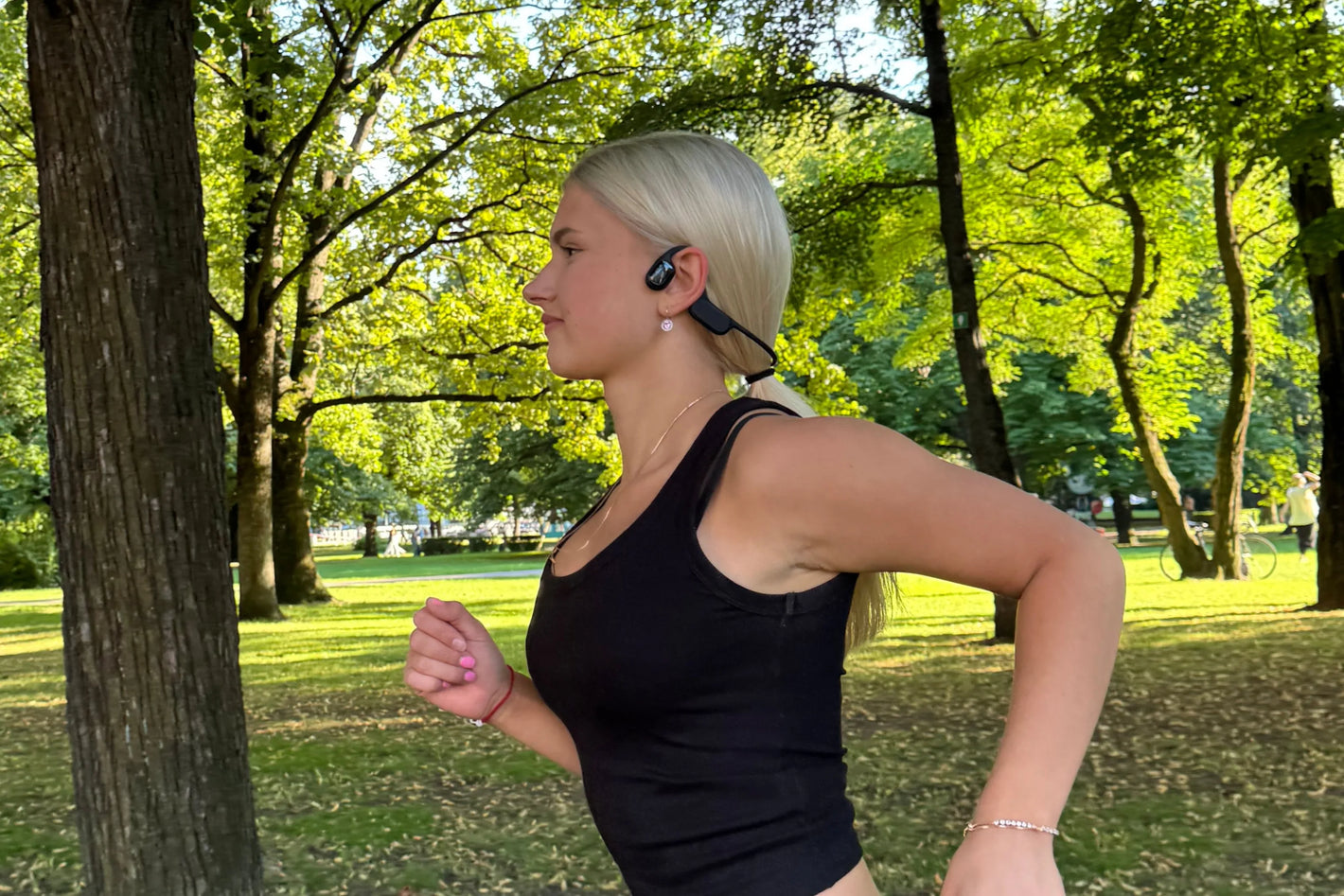 A girl running outdoors while wearing open-ear bone conduction headphones.