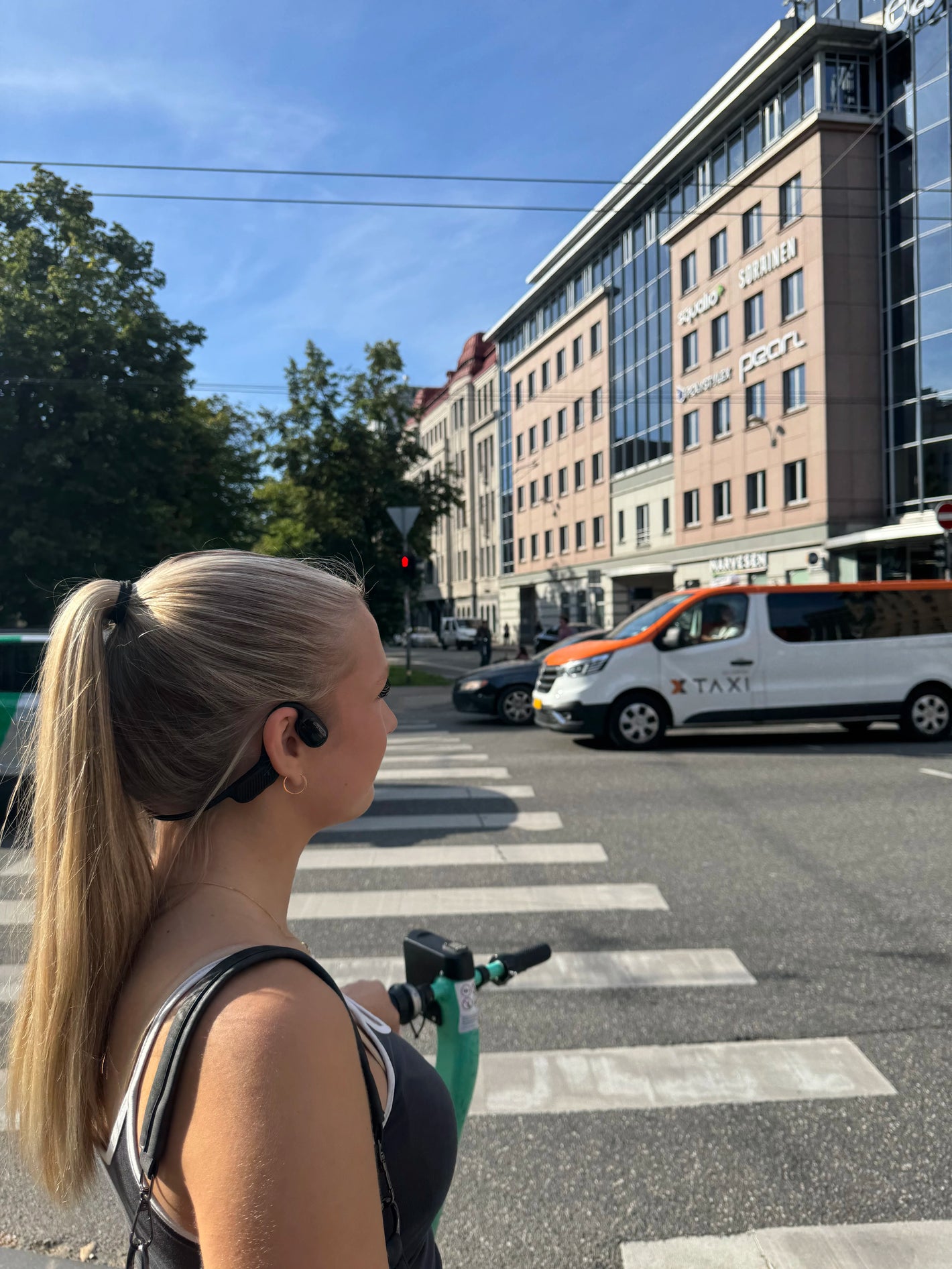 A girl wearing open-ear bone conduction headphones is aware of her surroundings in city traffic.
