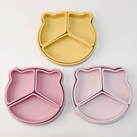 Collection of bear-shaped silicone baby plates in pastel colors including honey yellow, rose pink, and soft beige, featuring three divided sections and cute bear ear details for engaging mealtime experience