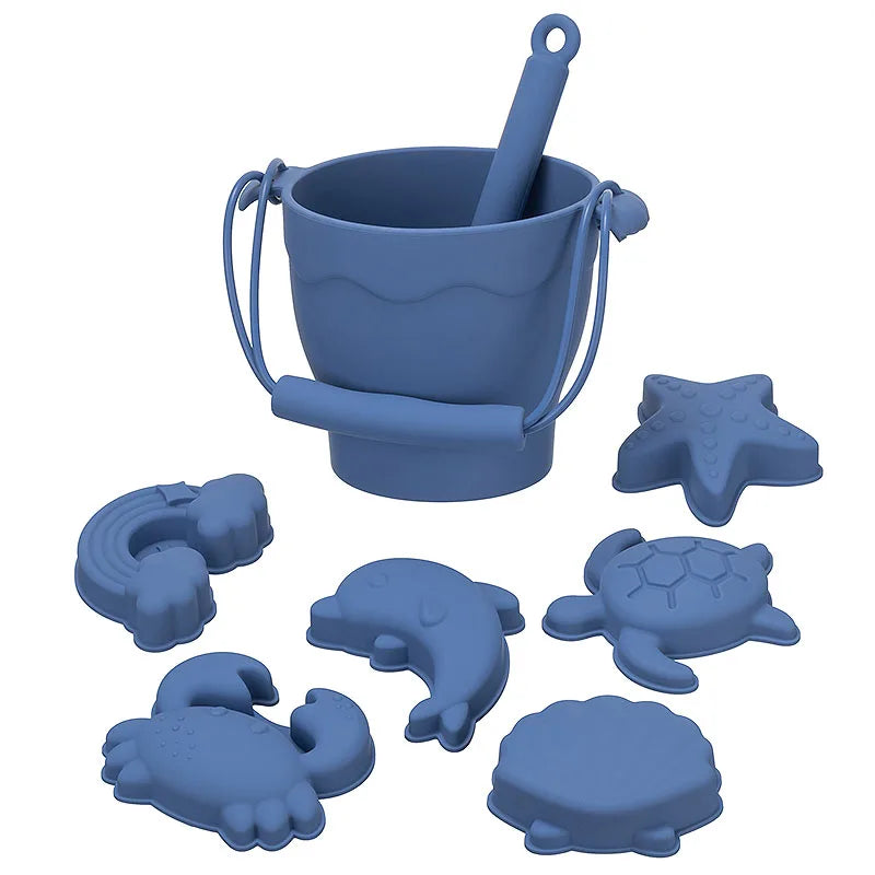 Complete dusty blue silicone beach toy set featuring a bucket with handle and scoop, plus six ocean-themed molds including turtle, starfish, shell, rainbow, crab, and dolphin shapes, perfect for sensory play at the beach or sandbox