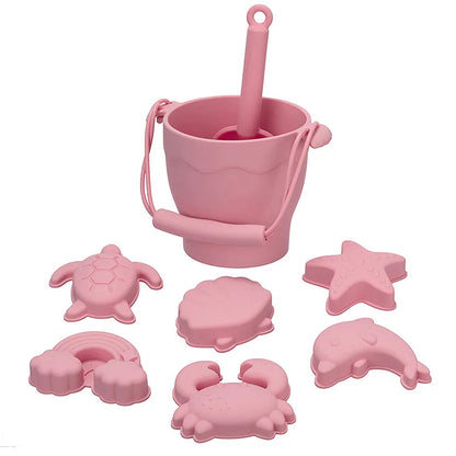 Complete pink silicone beach toy set featuring a bucket with handle and scoop, plus six sea-themed molds including turtle, starfish, shell, rainbow, crab, and dolphin shapes, perfect for safe and engaging sand play