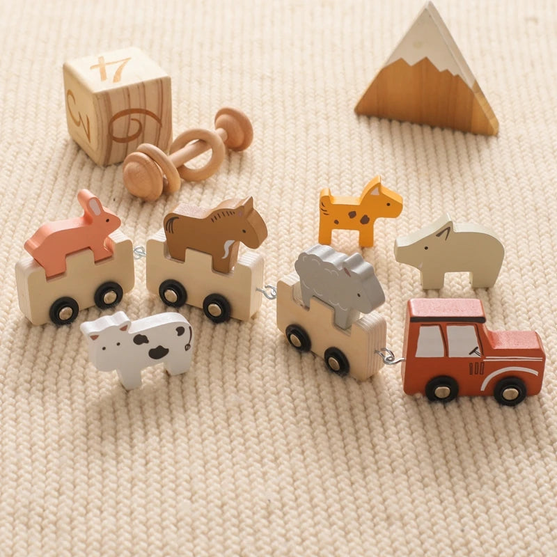 Collection of wooden toy train cars with safari animals including elephant, bear, giraffe, and polar bear riders, accompanied by natural wooden building blocks, snow-capped mountain, and mushroom accessories, arranged on cream textured fabric highlighting the earthy color palette and Scandinavian design