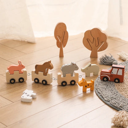 Wooden toy train set displayed on light wooden flooring with decorative brown trees and grey round rug, featuring a line of connected natural wood carriages with colorful animal riders including coral fox, brown horse, grey elephant, and beige bear, led by a red wooden locomotive, creating a cozy nursery scene