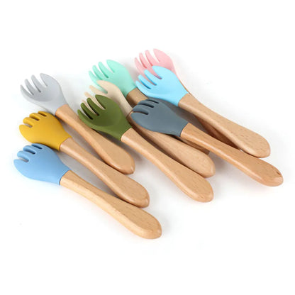 Collection of wooden baby forks with various colored silicone tips including mint, pink, blue, yellow, olive green, and grey, each featuring natural wooden handles and safe silicone prongs for comfortable infant feeding