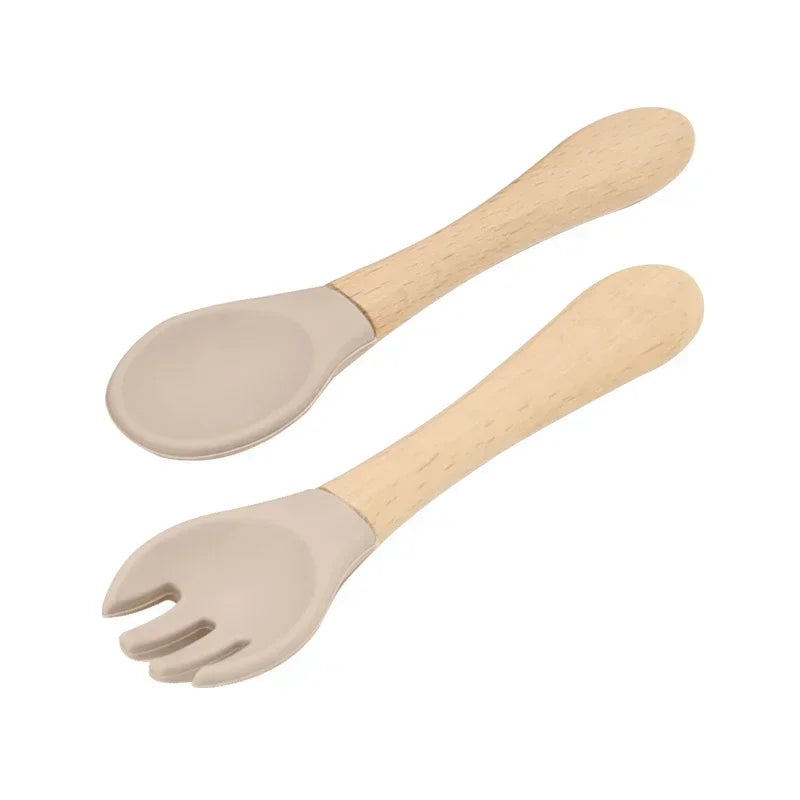 Set of natural wooden baby utensils featuring a spoon and fork with beige silicone tips, designed with smooth handles for easy grip and safe feeding