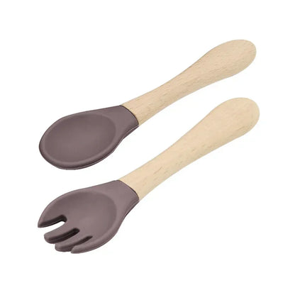 Set of natural wooden baby utensils featuring a spoon and fork with chocolate brown silicone tips, combining sustainable wooden handles with soft silicone ends for gentle and safe infant feeding