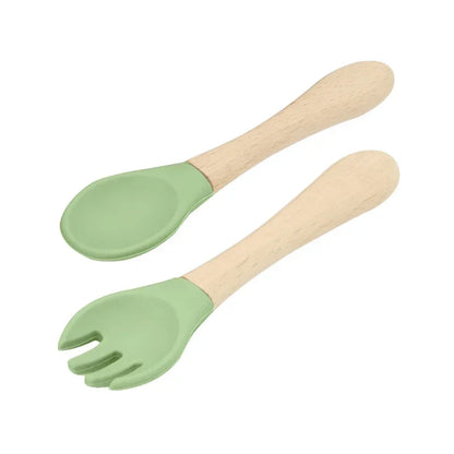 Set of natural wooden baby utensils featuring a spoon and fork with sage green silicone tips, combining natural wooden handles with soft silicone feeding ends for gentle and eco-friendly infant dining