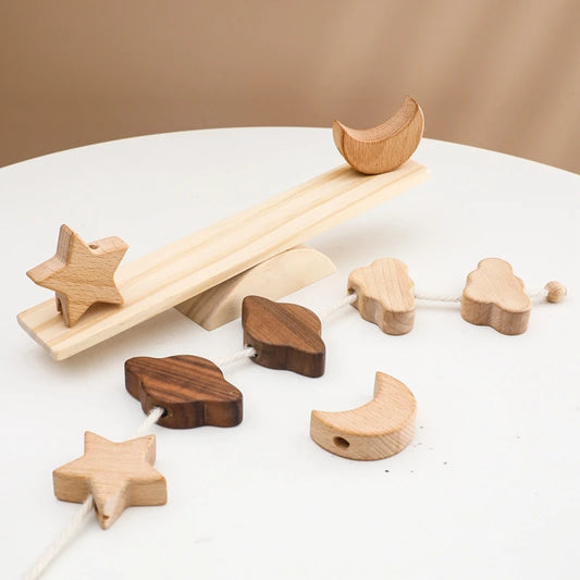 Montessori-inspired wooden balance beam toy with scattered celestial pieces including beech wood stars, crescent moons, and walnut wood clouds, displayed on white surface showing the complete set of interchangeable balancing elements and natural wood grain details