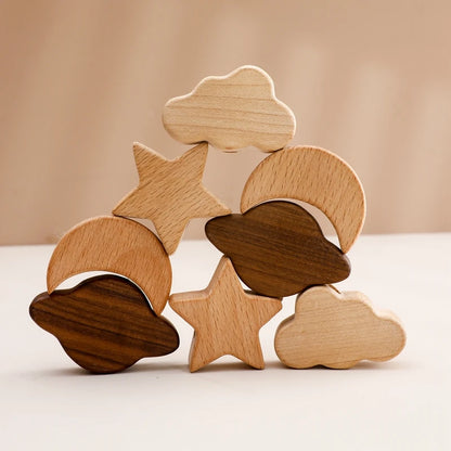 Artfully stacked celestial wooden toy pieces featuring beech wood stars, crescent moons, and clouds alongside contrasting walnut wood elements, arranged in a balanced composition showcasing the natural wood grain patterns and smooth finish against a warm neutral background