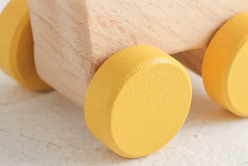 Close-up of a bright yellow wooden dinosaur car wheel component on a light textured surface, showcasing smooth rounded edges and child-safe matte finish