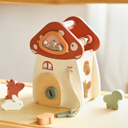 Close-up view of wooden mushroom house featuring a cream-colored base and terracotta red cap with inlaid gemstones in circular windows, accompanied by miniature woodland animal figures and geometric blocks, photographed in soft natural lighting highlighting the enchanting details