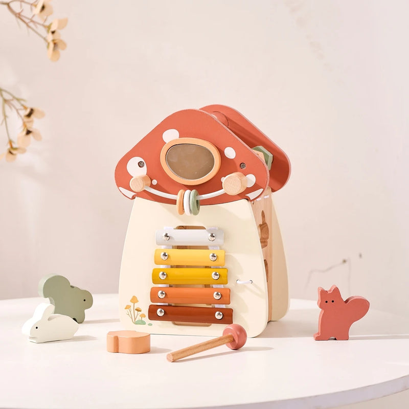 Complete wooden mushroom house music set featuring a gradient xylophone from yellow to terracotta, wooden mallet, terracotta red polka-dotted cap with gemstone window, and charming woodland animal figures including white rabbit, grey squirrel, and coral fox, arranged on white surface with dried botanical accents