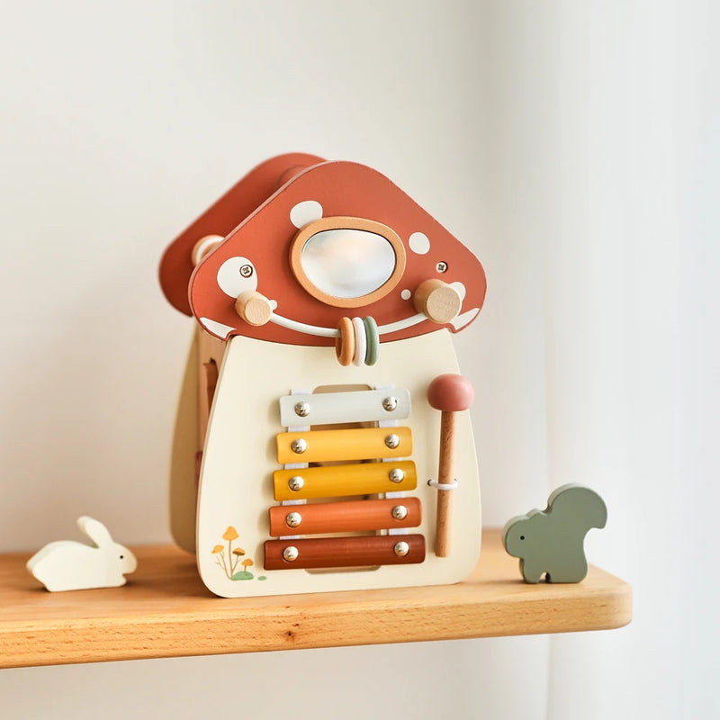 Musical wooden mushroom house featuring a built-in rainbow xylophone with graduated warm tones from yellow to terracotta, decorated with white polka dots on red cap, accompanied by white rabbit and grey squirrel figures on natural wooden shelf, perfect for sensory play